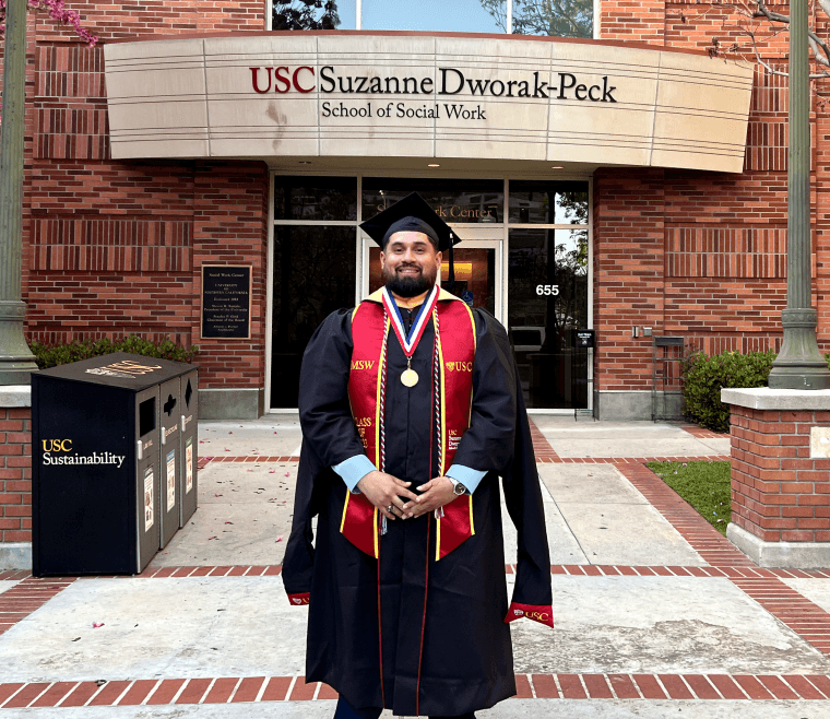 Image of a man standing Infront of a building in graduation cap