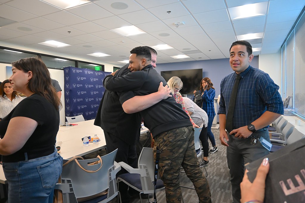 Marine Corps veteran George Casillas hugs a participant during a Suicide Prevention Month Coffee Chat, surrounded by attendees in the Stephen A. Cohen Clinic.