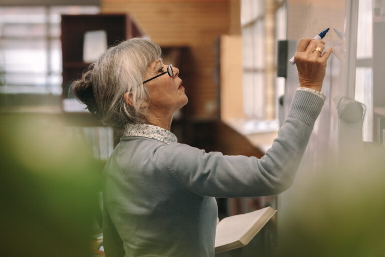 Woman with gray hair, writing on a white board