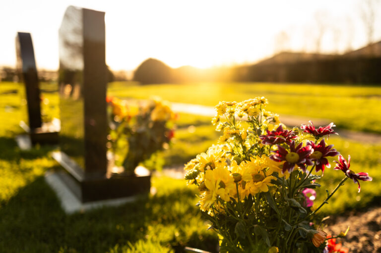 Photo of a cemetery with a vibrant sunset in the background and flowers in the foreground