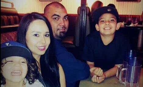Lolita Olivarez sits with her husband, a Marine Corps Veteran, and their two young children at a restaurant table, smiling together as a family.