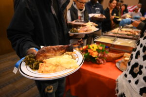 Someone holds a plate of Thanksgiving food on a plate as people in line behind are served food.