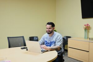 Veteran services officer Joel Luna sits smiling at a desk, working on processing claims on his computer.