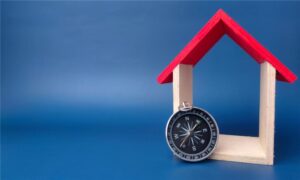 Small wooden house frame with a red roof sheltering a compass, symbolizing guidance and direction.